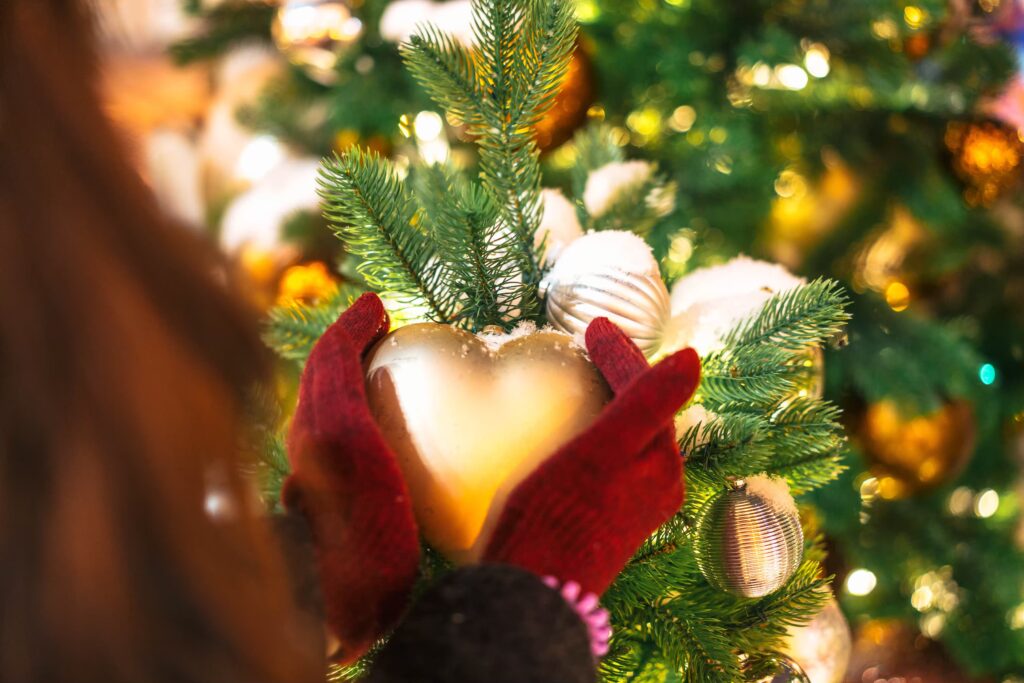 Lady holding a heart shaped bauble on a Christmas tree.