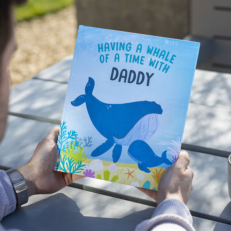 Man holding Having a Whale of a Time with daddy book. The cover features a daddy and baby whale.