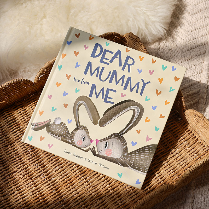 Playful cover of a baby and mummy bunny nose to nose and ears together shaped as a heart. The book rests on a wicker tray with soft sheepskin rug behind it.